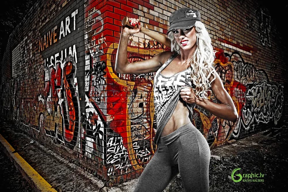 Fitnesa modele sporta apģērbā pozē ar beisbola nūju pie grafiti sienas